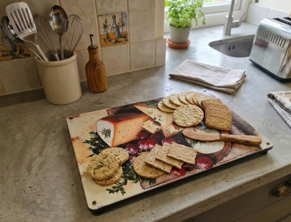 Decorative metal cheeseboard with cheeses image on it and crackers/biscuits on top of it, sitting on top of a kitchen counter.