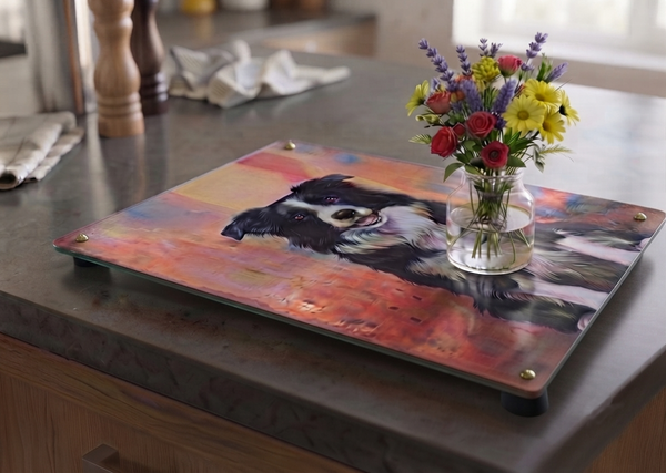 a Vintage style metal sign used as a display plinth, with an image on it of a Border Collie in a sitting pose. This plinth has a small glass vase of fresh flowers on it. 