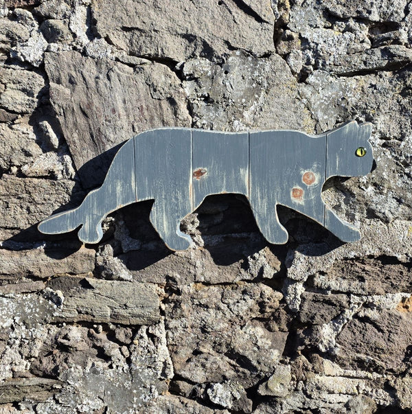 Stalking cat wooden wall art displayed on a stone wall