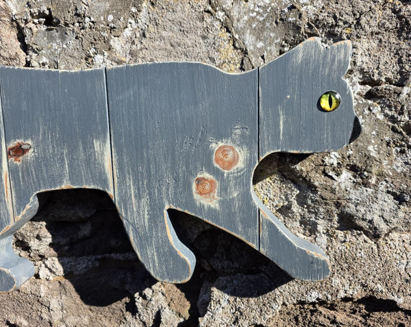 Close up view of a Stalking cat rustic wooden wall art displayed on a stone wall 