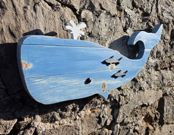 Blue whale wooden wall art displayed on a stone wall viewed at an angle