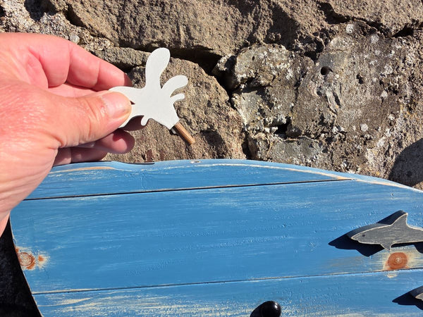 Blue whale rustic wooden wall art displayed on a stone wall with a close up of a hand holding the white coloured blowhole piece