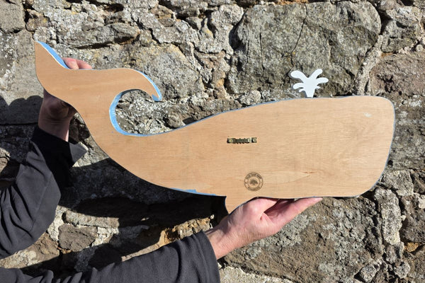Reverse side of Blue whale wooden wall art being held for sizing against a stone wall