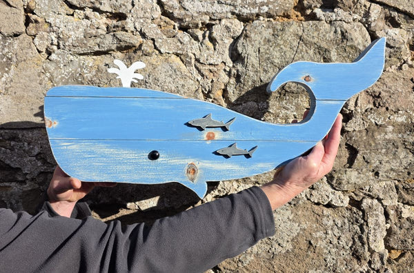 Blue whale wooden wall art being held for sizing against a stone wall