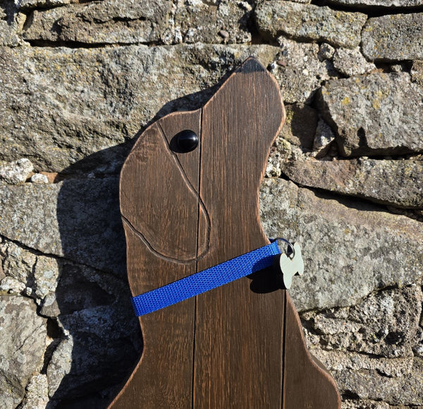 Close up view of Wooden Labrador Retriever wearing a blue decorative collar wall art against a stone wall