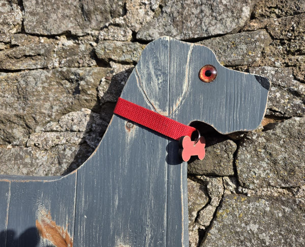 Wooden Great Dane dog with a red collar & dog tag against a stone wall