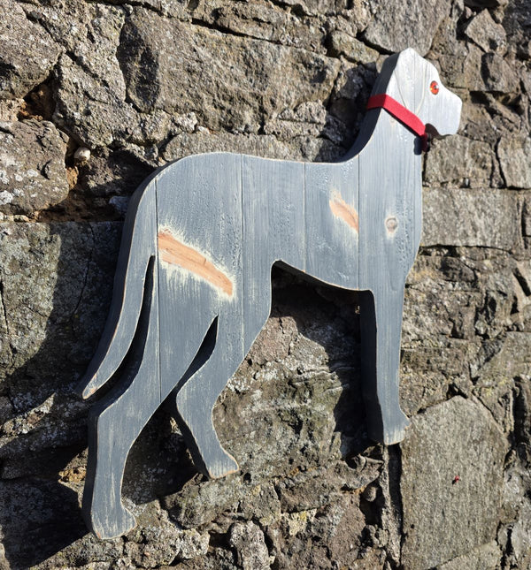 Siided view of a Wooden Great Dane dog with a red collar against a stone wall