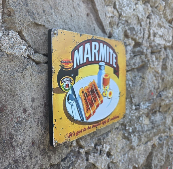 Vintage-style metal sign with Marmite image on it, hanging on a stone wall viewed at an angle