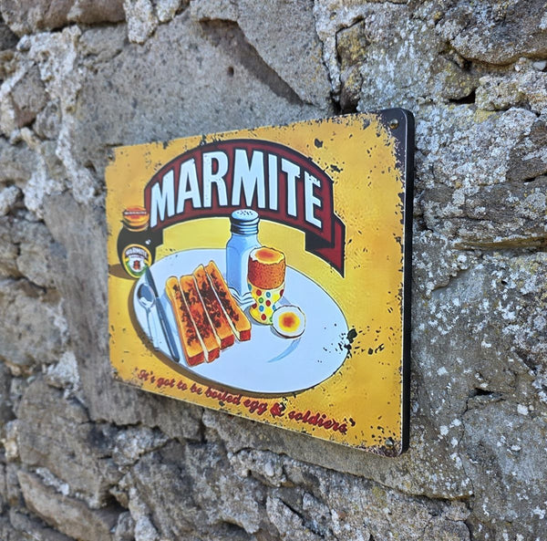Vintage-style metal sign with Marmite image on it, hanging on a stone wall viewed at another angle