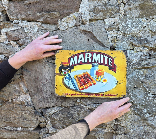 Vintage style Marmite sign on a stone wall with hands holding it showing its size