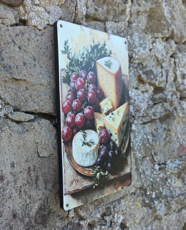 A side view of a decorative vintage style metal sign (repro) hanging on a stone wall with an image of cheeses and grapes on a cheeseboard