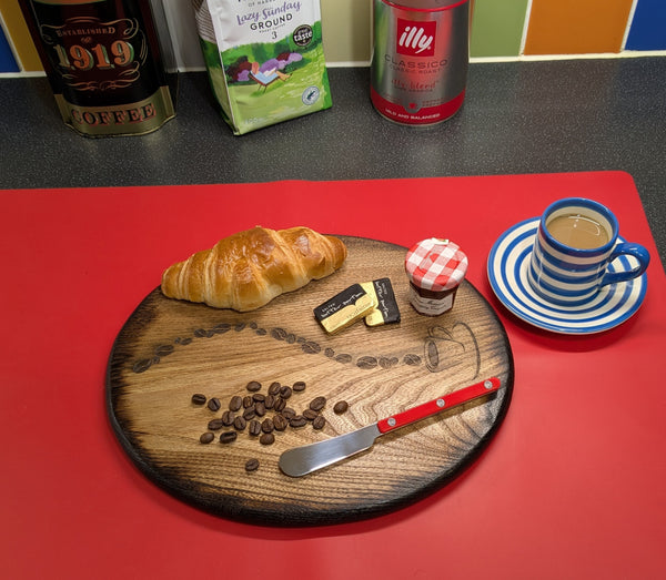 Ash wood 'Coffee Bean style' serving board displayed with croissant, butter, jam & funky red butter knife along side a cup of coffee