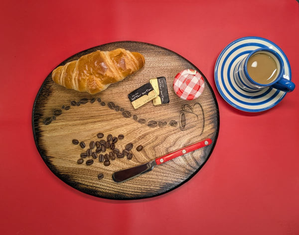 Ash wood 'Coffee Bean style' serving board displayed with croissant, butter, jam & funky red butter knife along side a cup of coffee overhead view
