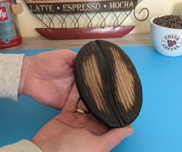 Small ash wood coffee bean being held to show sizing