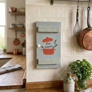 Vintage style shabby chic, sage green pine wall art shutter hanging on a Farmhouse kitchen wall, with a design on it of a red crock-pot & lid, along with the words 